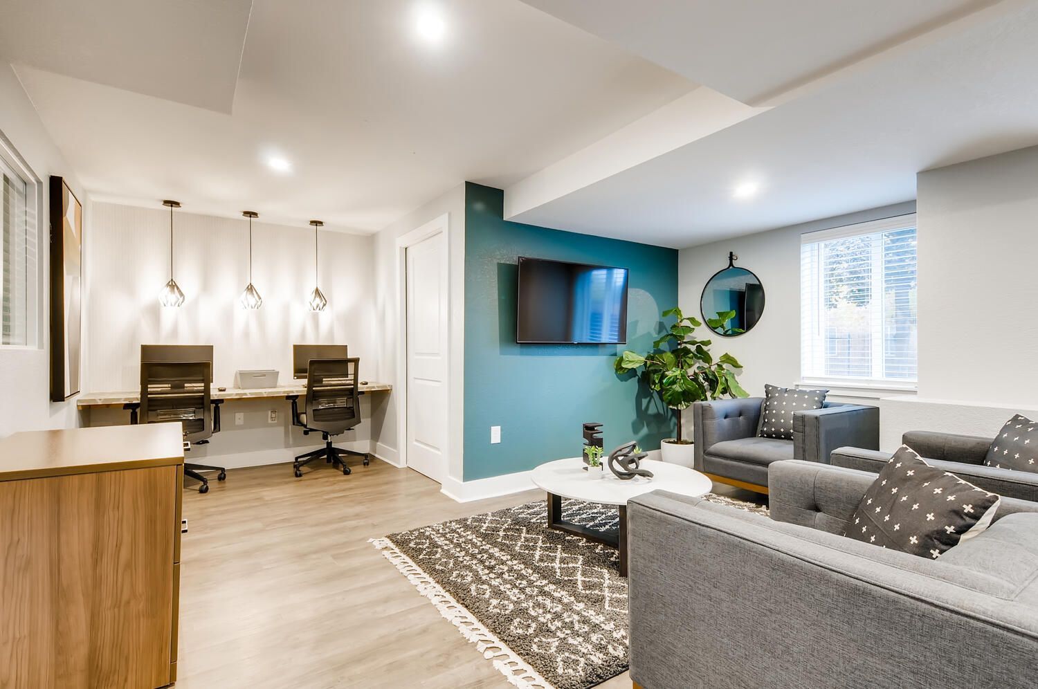 Resident lounge with teal accent wall, wall-mounted TV, plants, and gray seating.