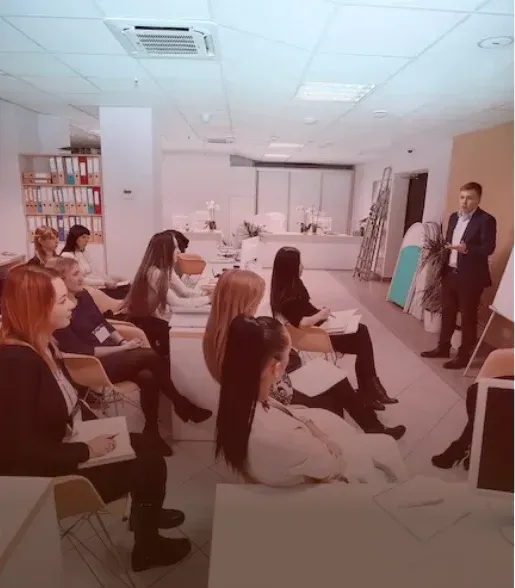 Office meeting with people seated facing a presenter at the front of a conference room.