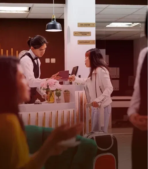 Two people exchange papers at a hospital or clinic reception desk under warm indoor lighting.