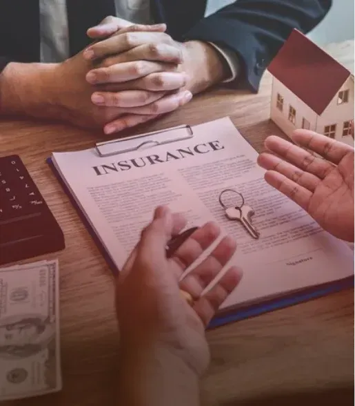 Hands discussing an insurance document on a desk beside a small house model and money