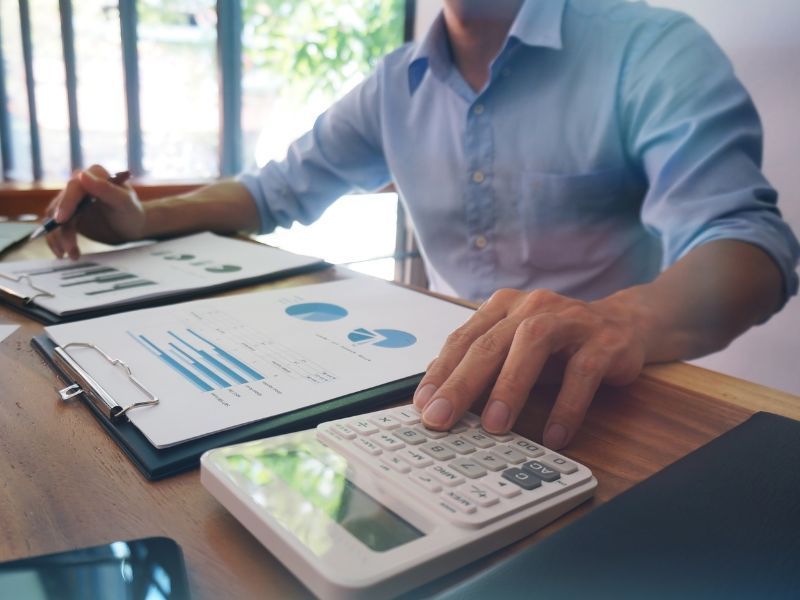 Person using a calculator beside financial charts on a desk in a bright office