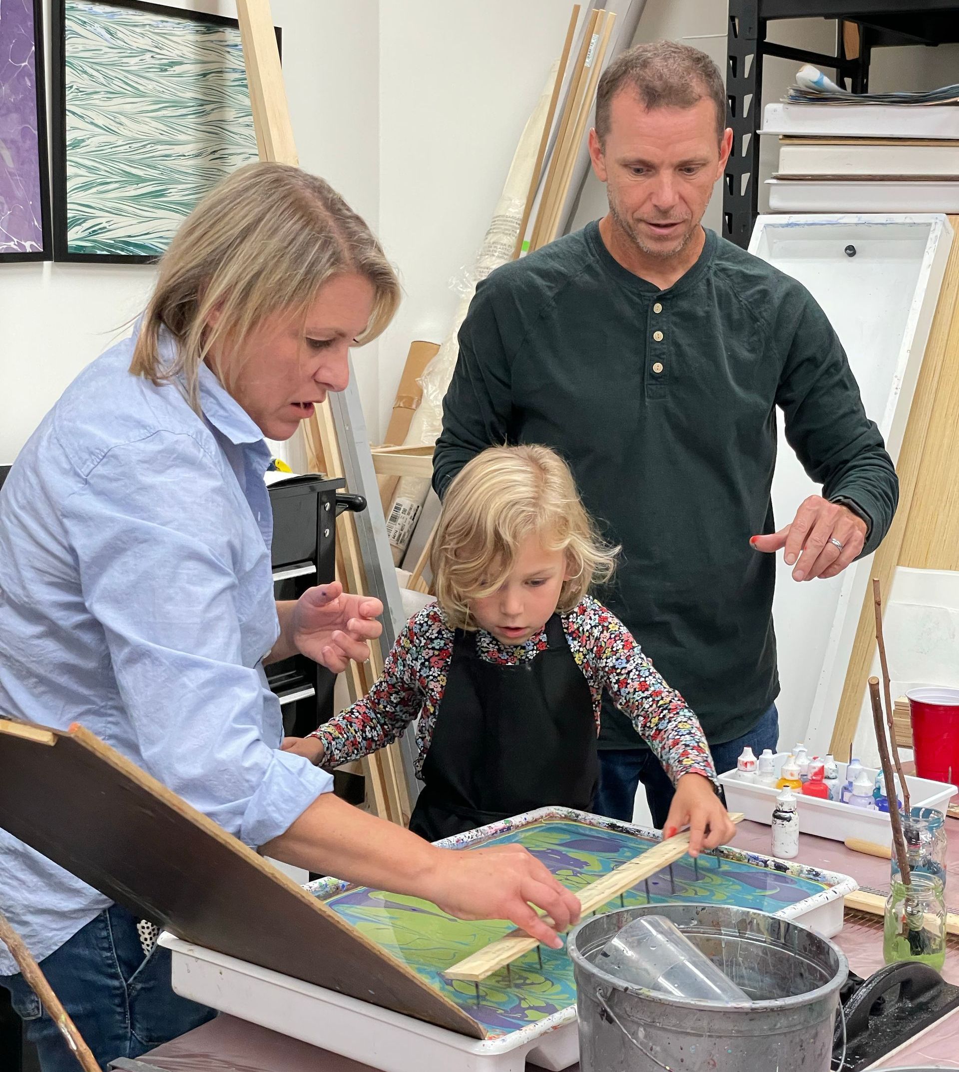 Man and Woman stand in anticipation as their daughter is amazed, creating her own artwork.