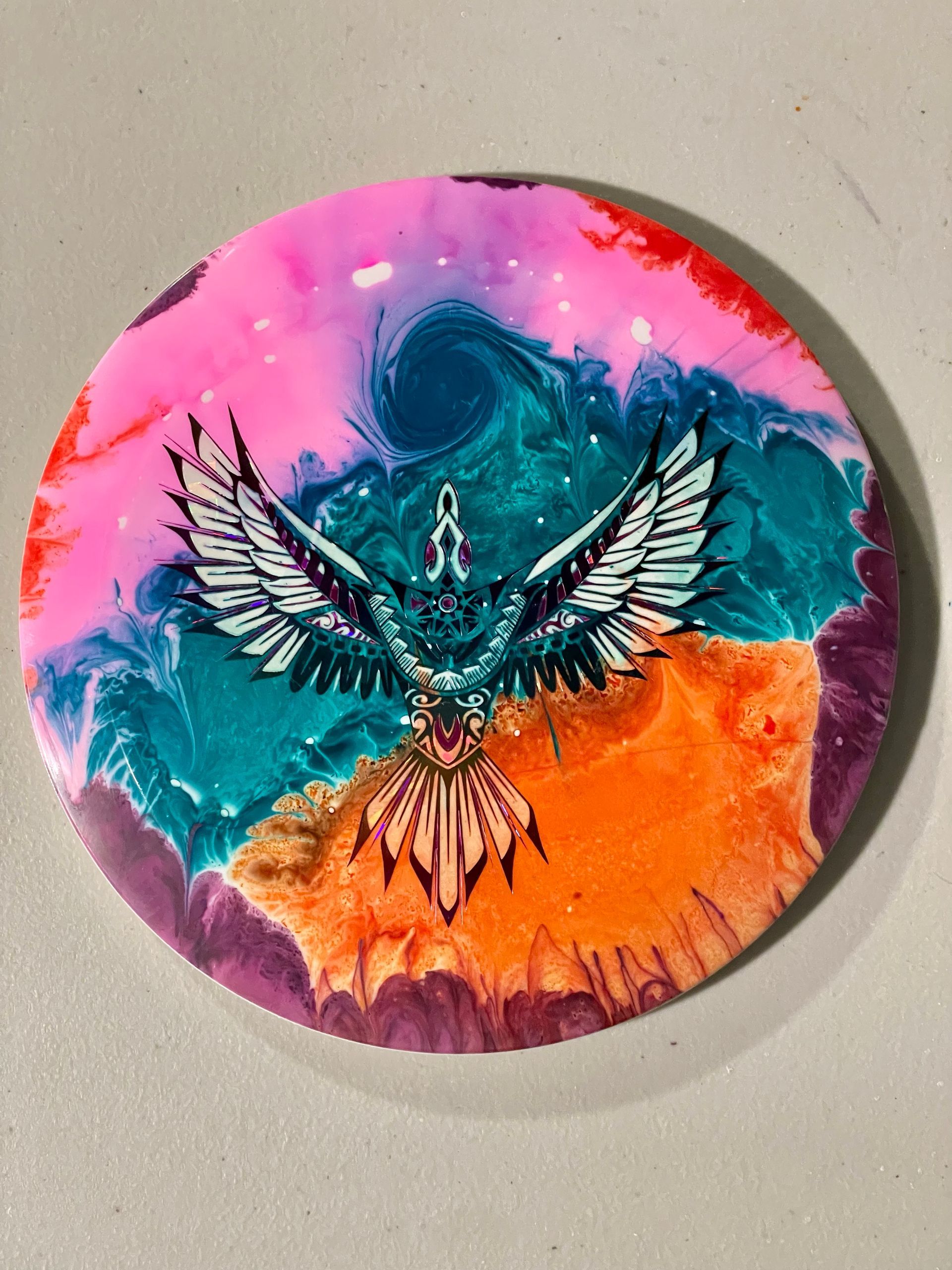 Dyed disc in spiking colors of orange, teal, and pink over a bird stamp.