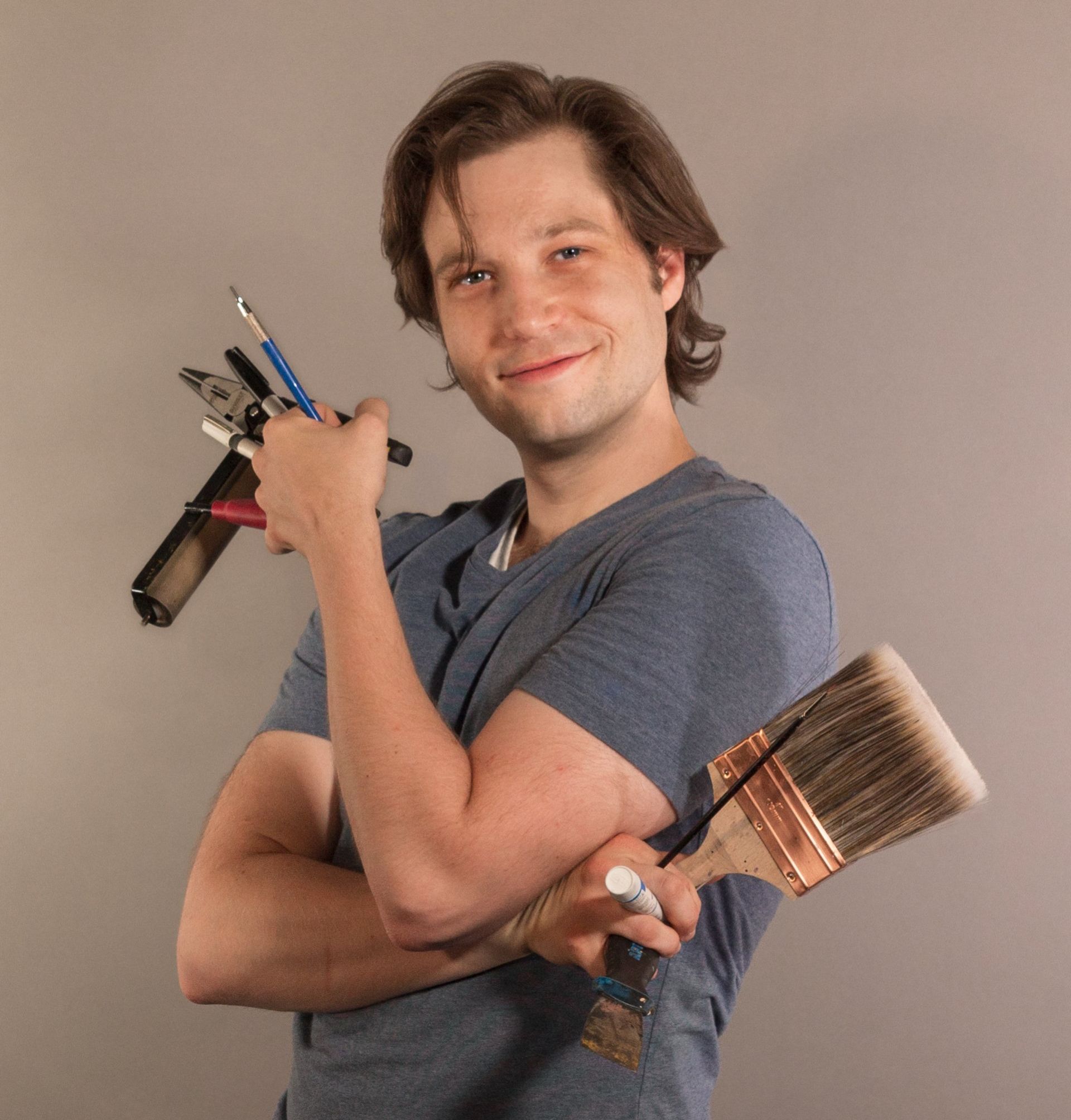 Photo portrait of Keith Garubba holding lots of art tools and supplies in both hands.