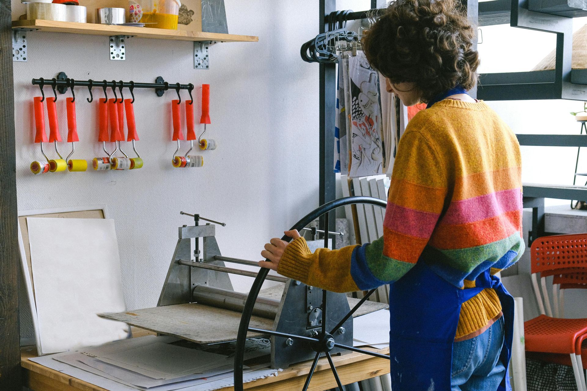 Artist turns the crank on a printing press while making her design.