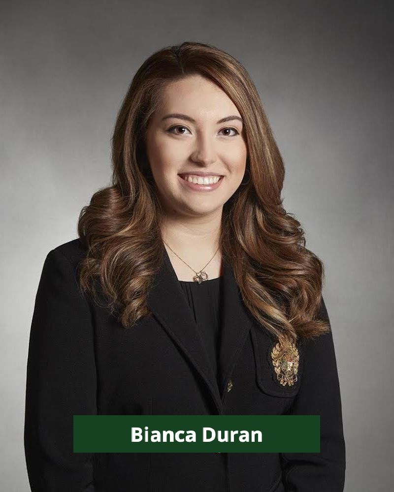 Bianca Duran smiles, wearing a black blazer, against a gray backdrop.