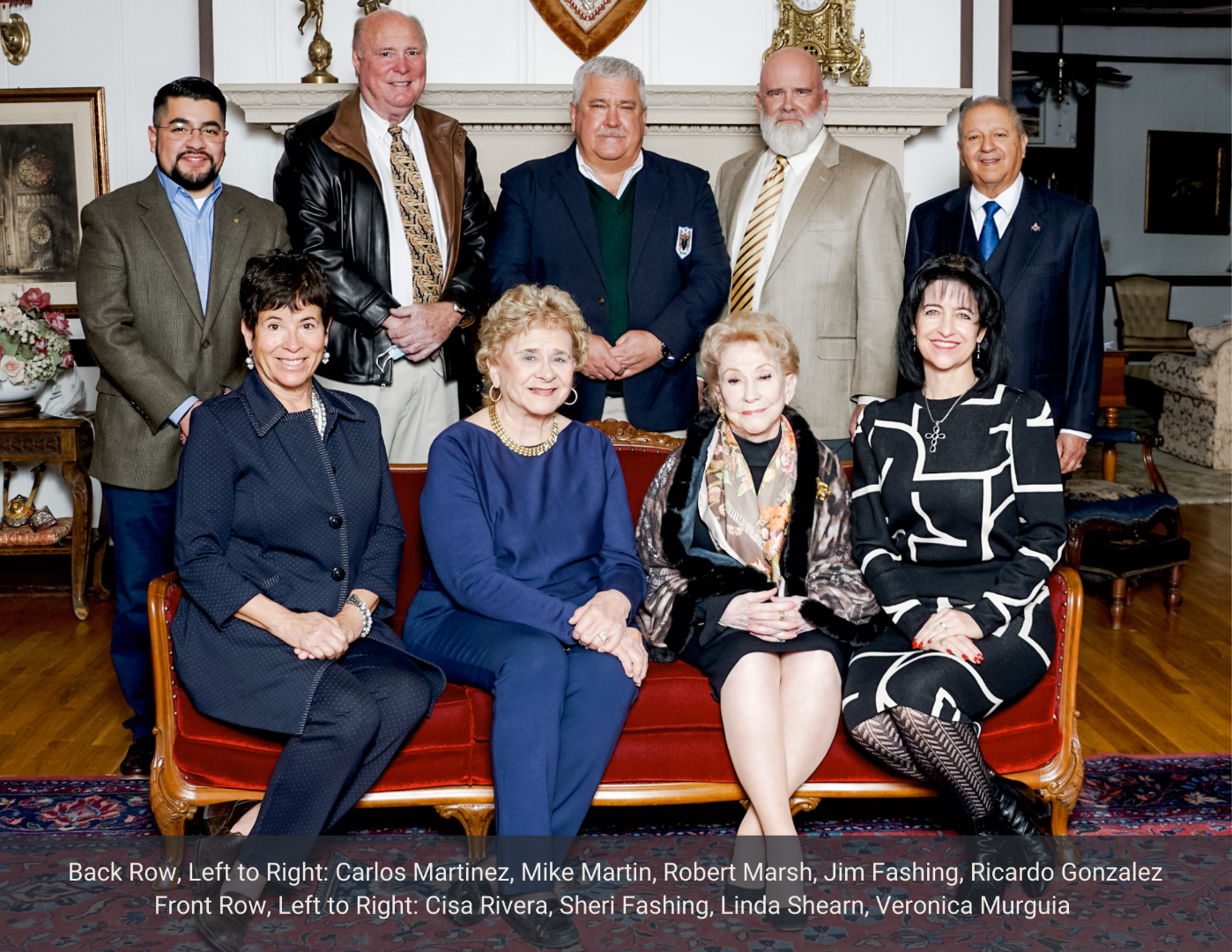 Group photo of well-dressed people, seated and standing in a room.