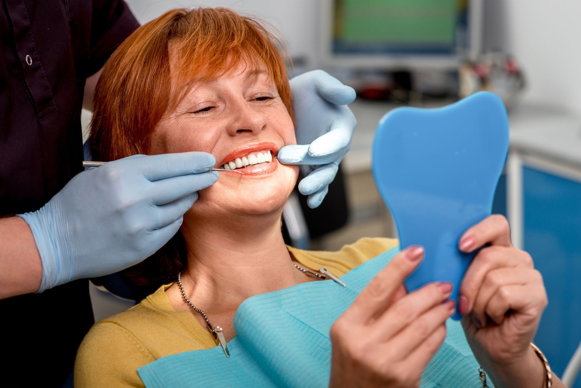 Dental exam as gloved hands adjust teeth while patient views smile in a hand mirror. Dental exam as gloved hands adjust teeth while patient views smile in a hand mirror.