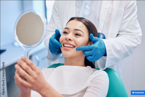 Person in dental chair holding mirror while dentist adjusts alignment with gloved hands.