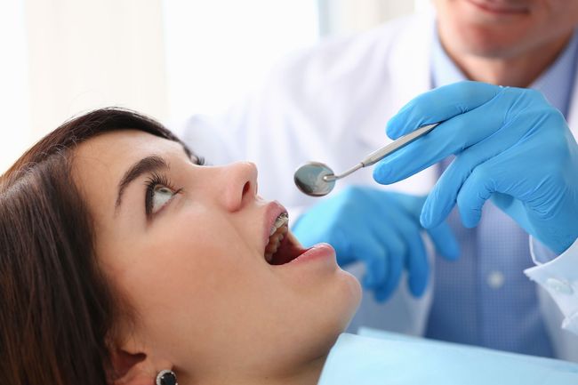 Dentist examining patient teeth with mirror during routine dental checkup in modern clinic.