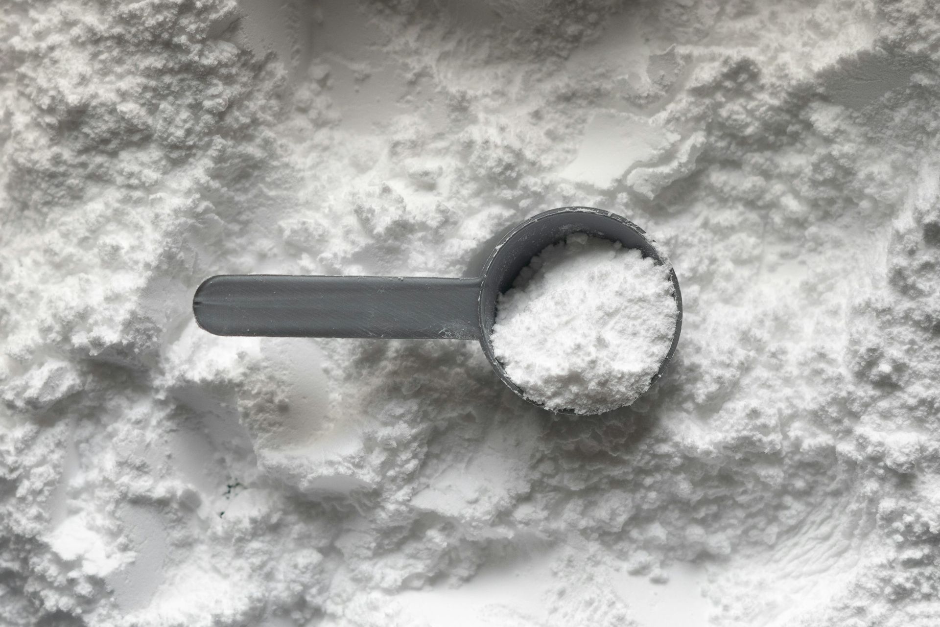 A grey scoop filled with white creatine monohydrate powder