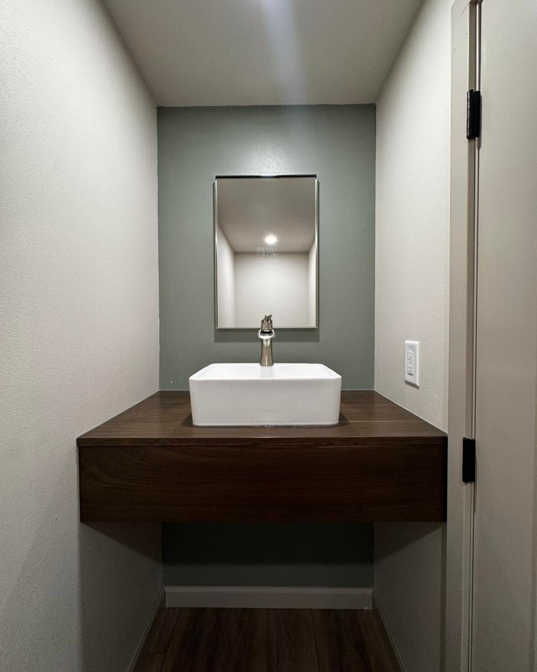 Modern bathroom vanity with white sink, rectangular mirror, and dark wood countertop in a narrow alcove