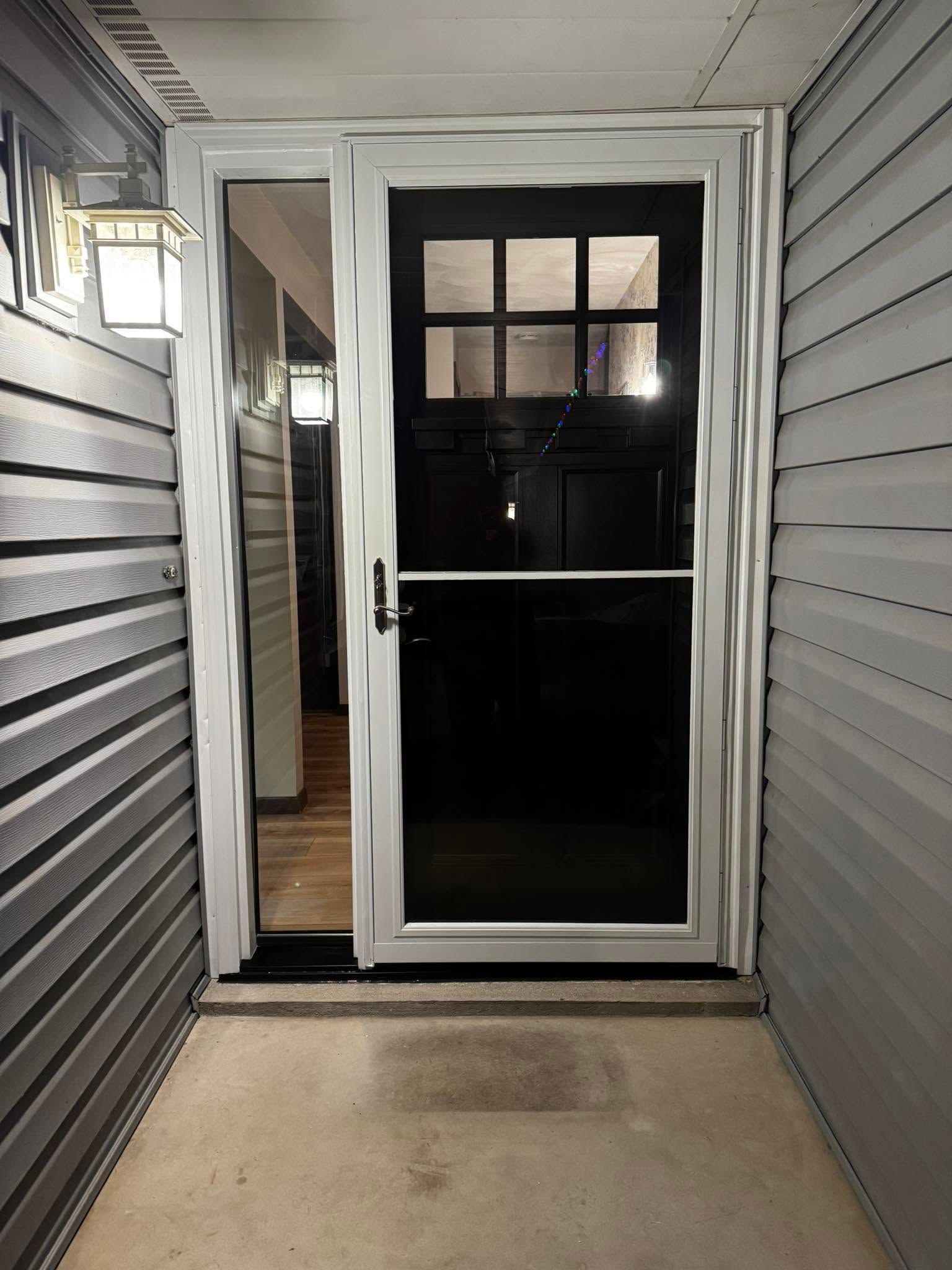 Narrow front porch with gray siding and a white storm door leading into a dark interior.