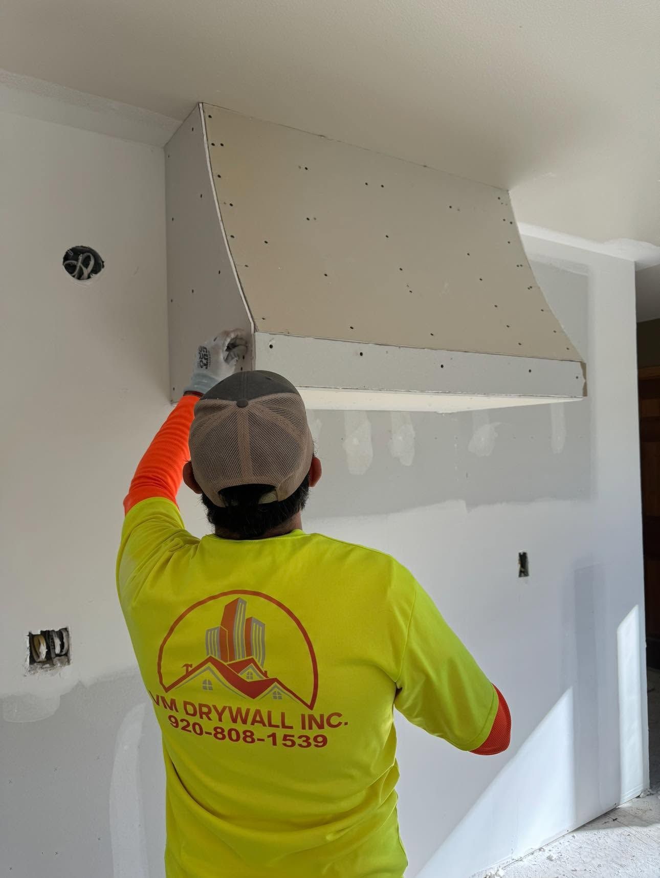 Worker in neon shirt installing drywall panel in a room under construction.