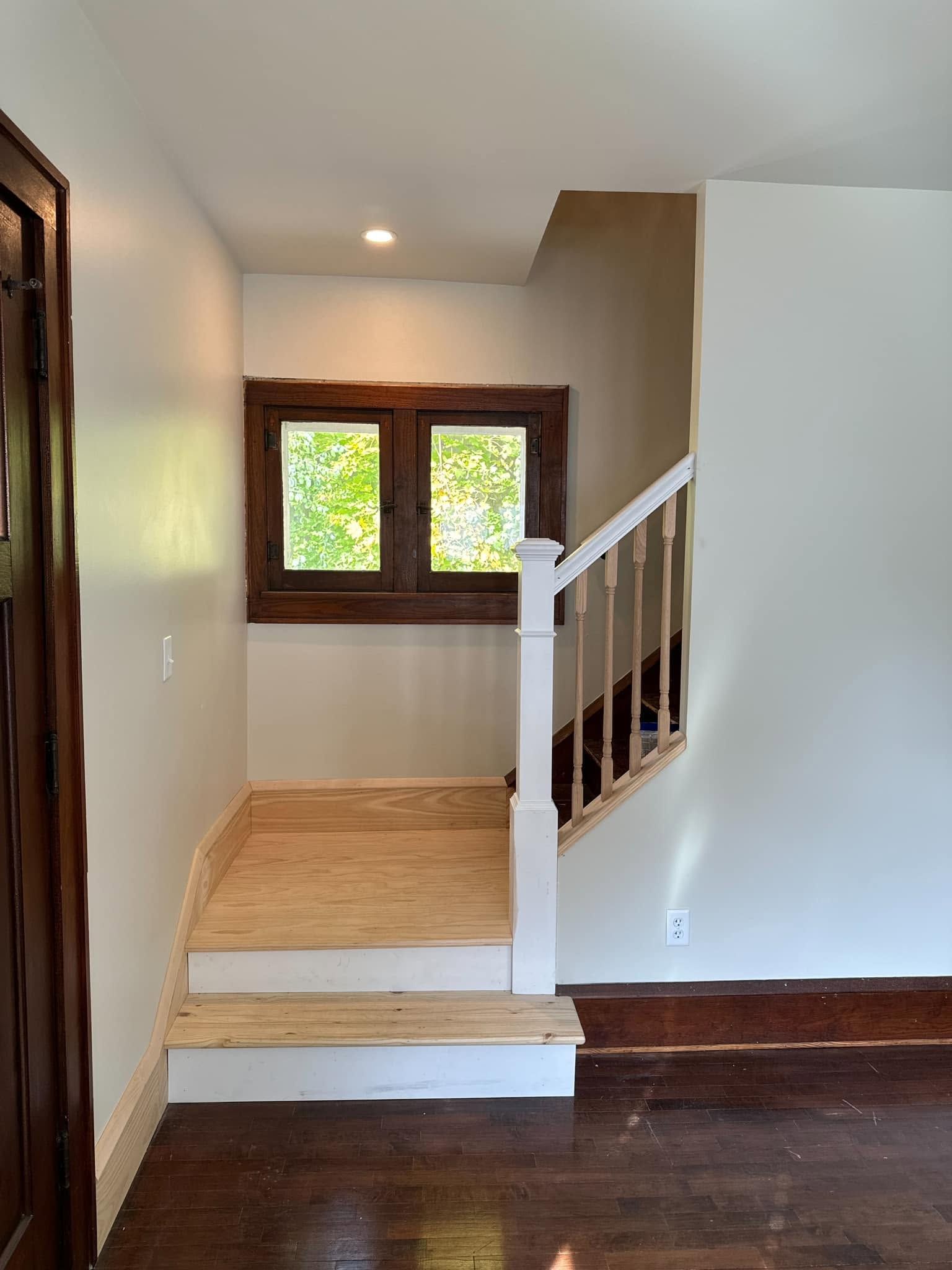 Interior hallway with a small wooden step-up landing, staircase railing, and two wood-trimmed windows.