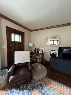 Living room with brown leather chair, ottoman, TV stand, wood door, and blue patterned rug