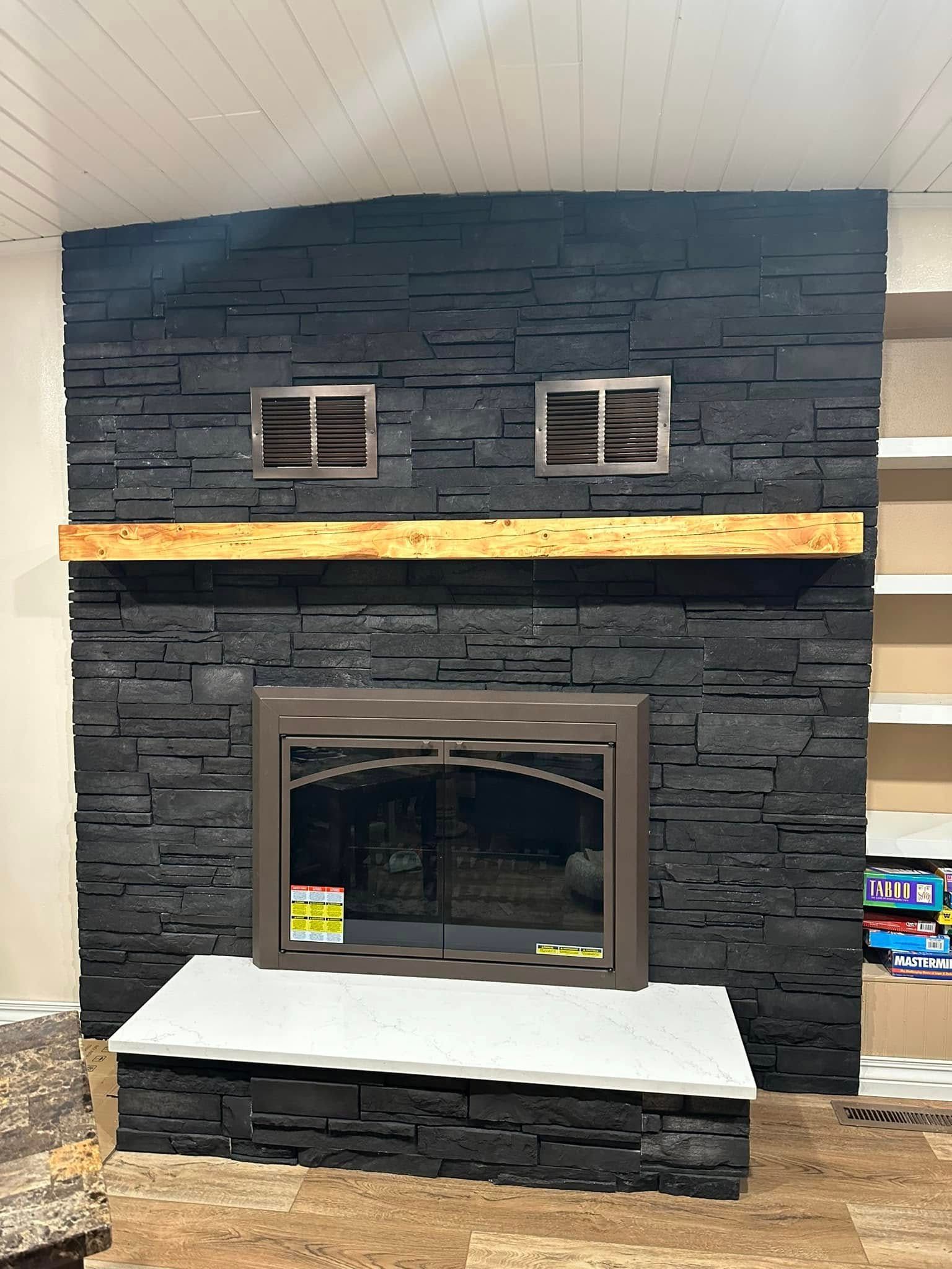Modern black stone fireplace with two vents, a wooden mantel, and white hearth in a showroom.