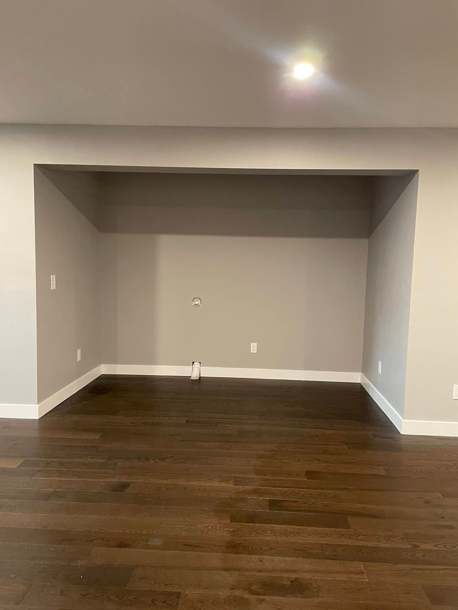 Empty gray recessed alcove in a room with dark hardwood floors and white trim.
