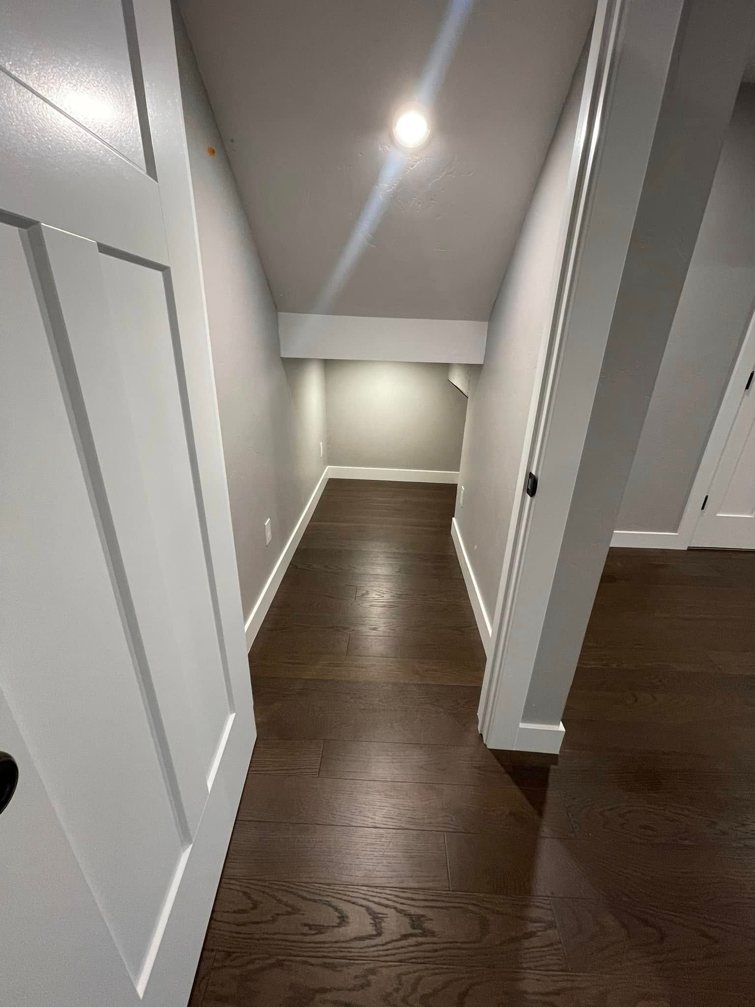 Empty hallway with dark wood floor, white walls, and recessed ceiling lights.