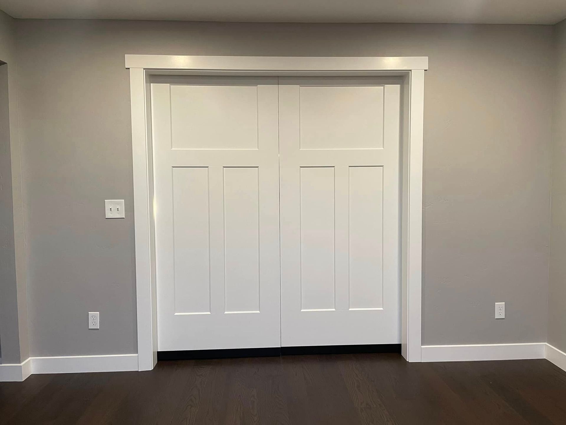 White double closet doors in a gray room with dark wood flooring.