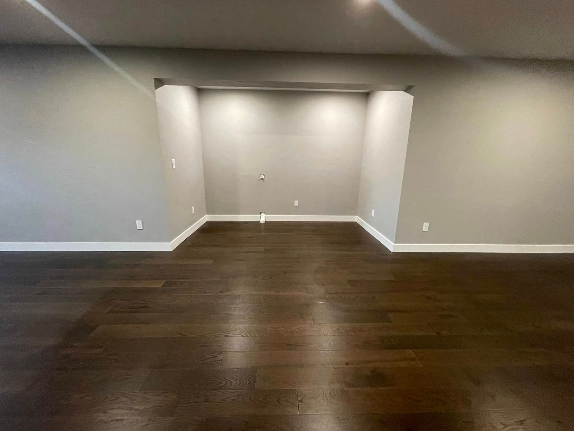 Empty room with dark wood floors, light gray walls, and a recessed alcove with spotlights.