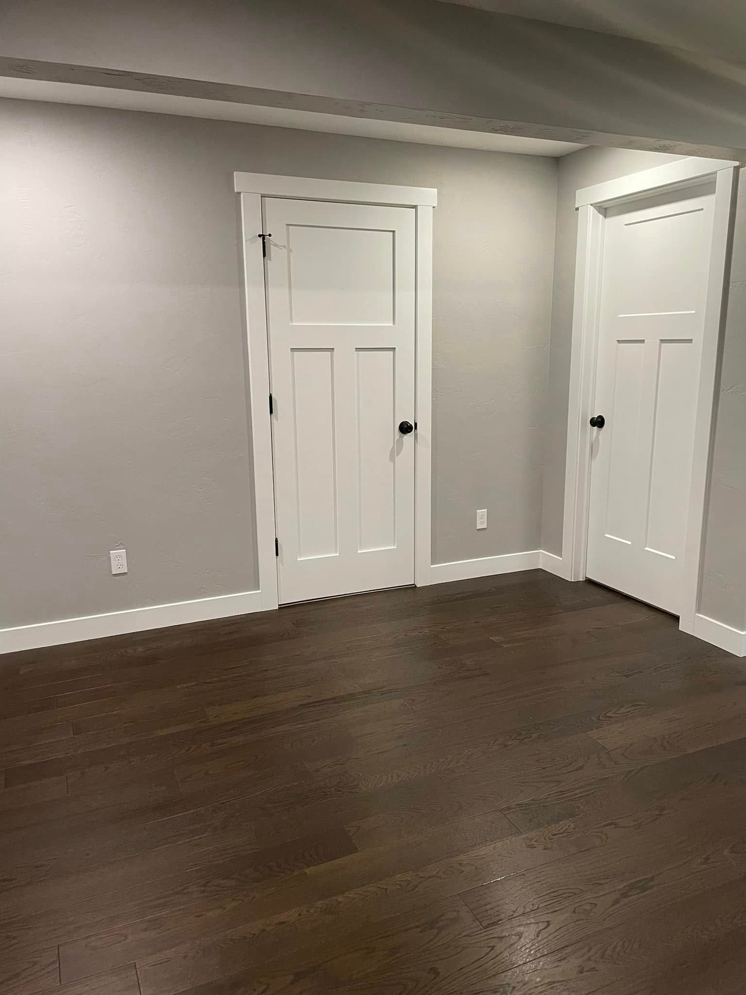 Empty room with gray walls, dark wood floor, and two white doors.