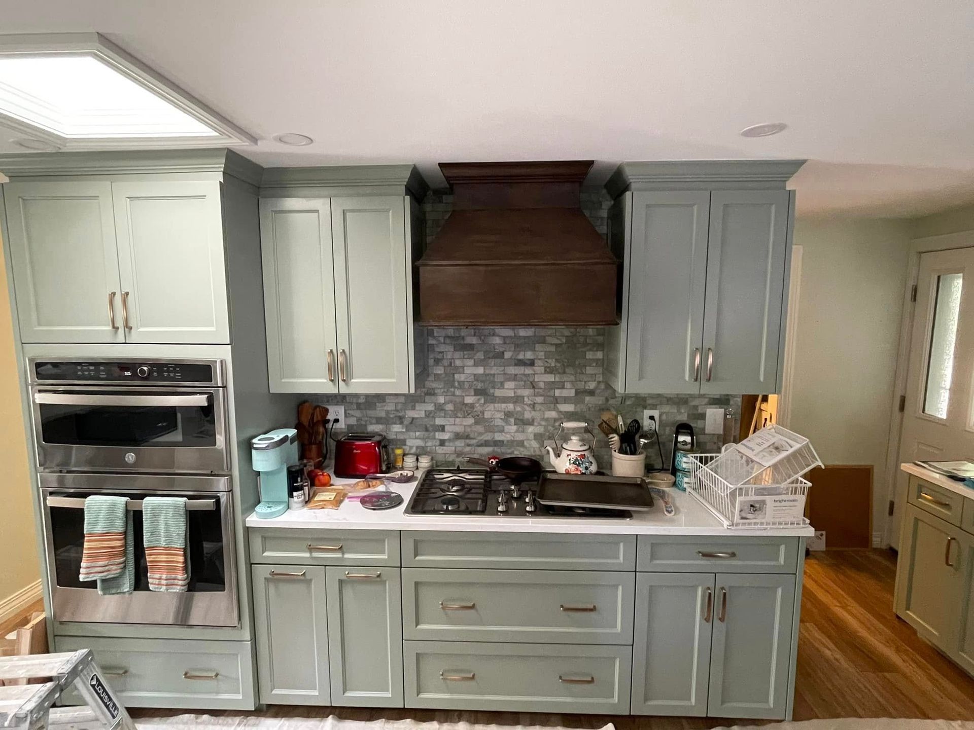 Bright kitchen with gray cabinets, stainless oven, mosaic backsplash, and wood flooring