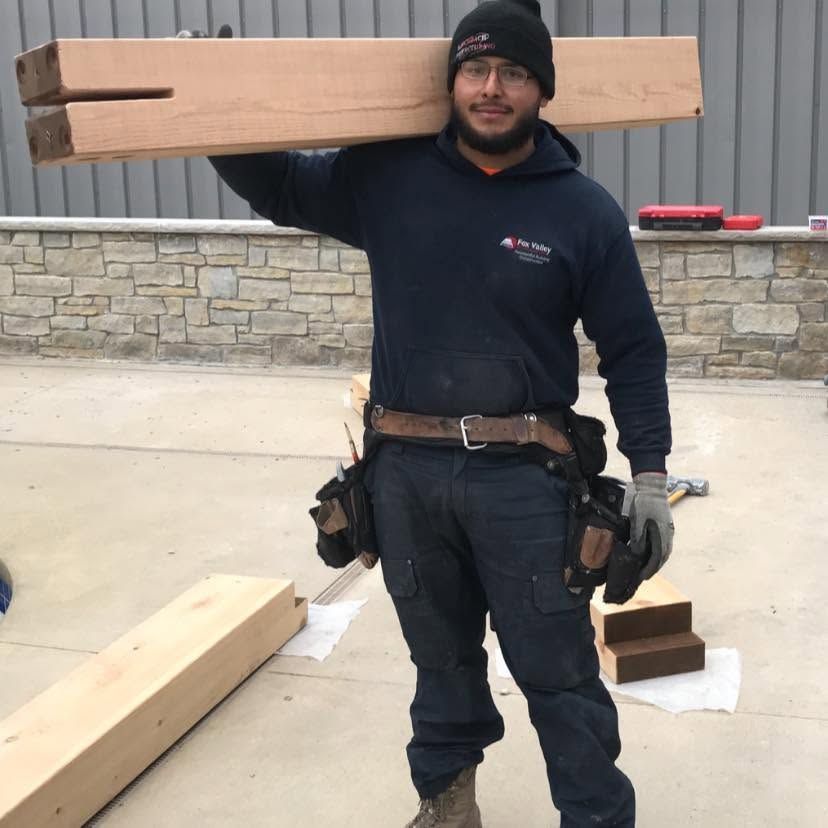 Worker carrying a long wooden beam on his shoulder at a construction site