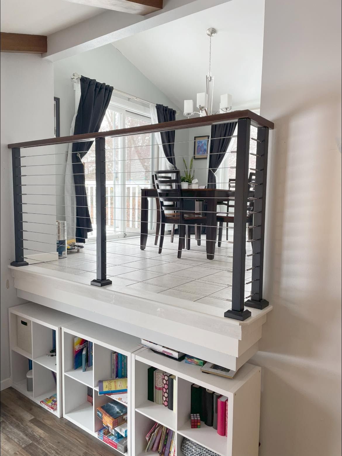 Dining area with black railing balcony above white cubby shelves in a bright modern home