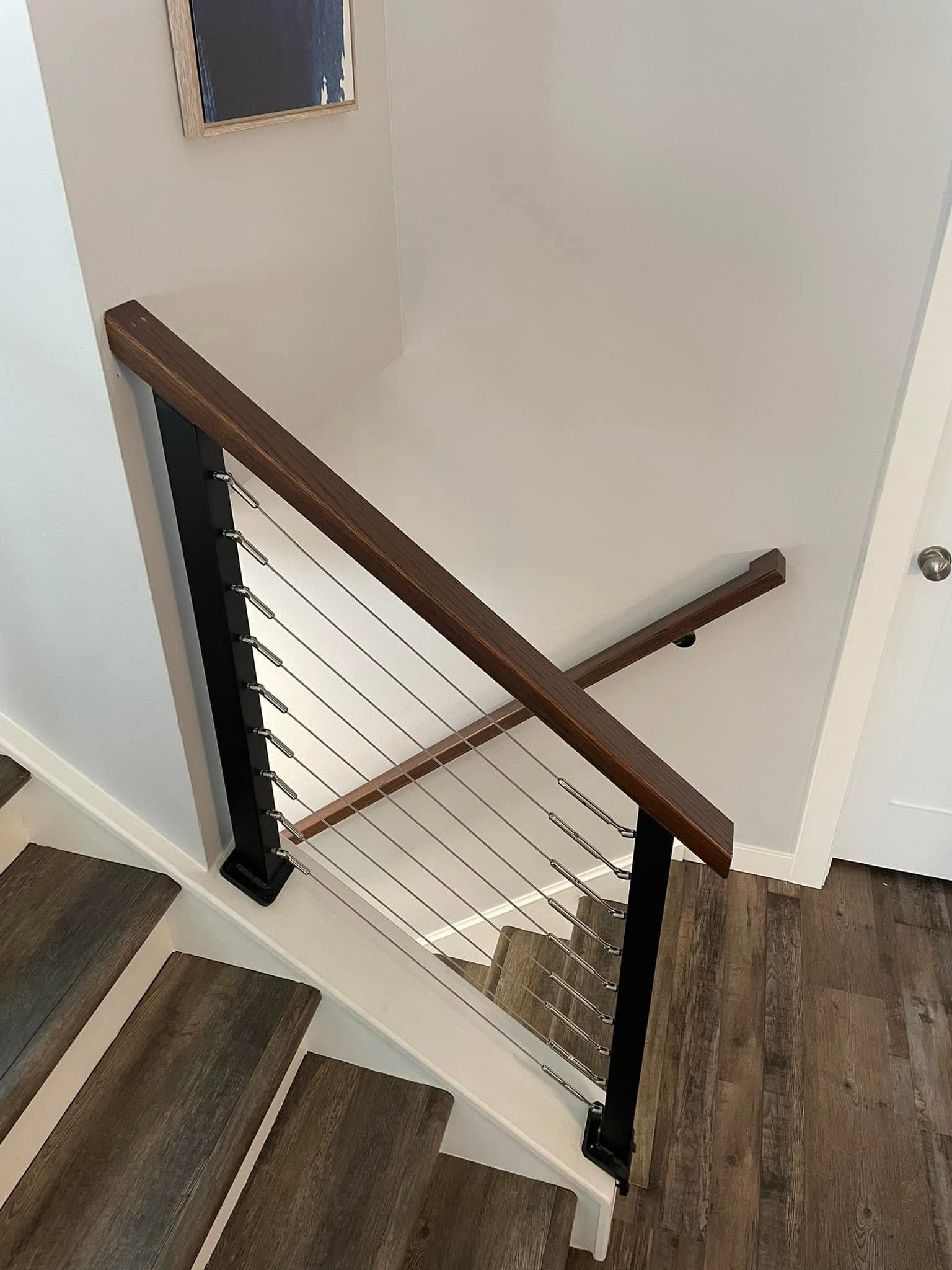 Stairwell with wood handrail, white walls, and a modern cable railing beside carpeted steps