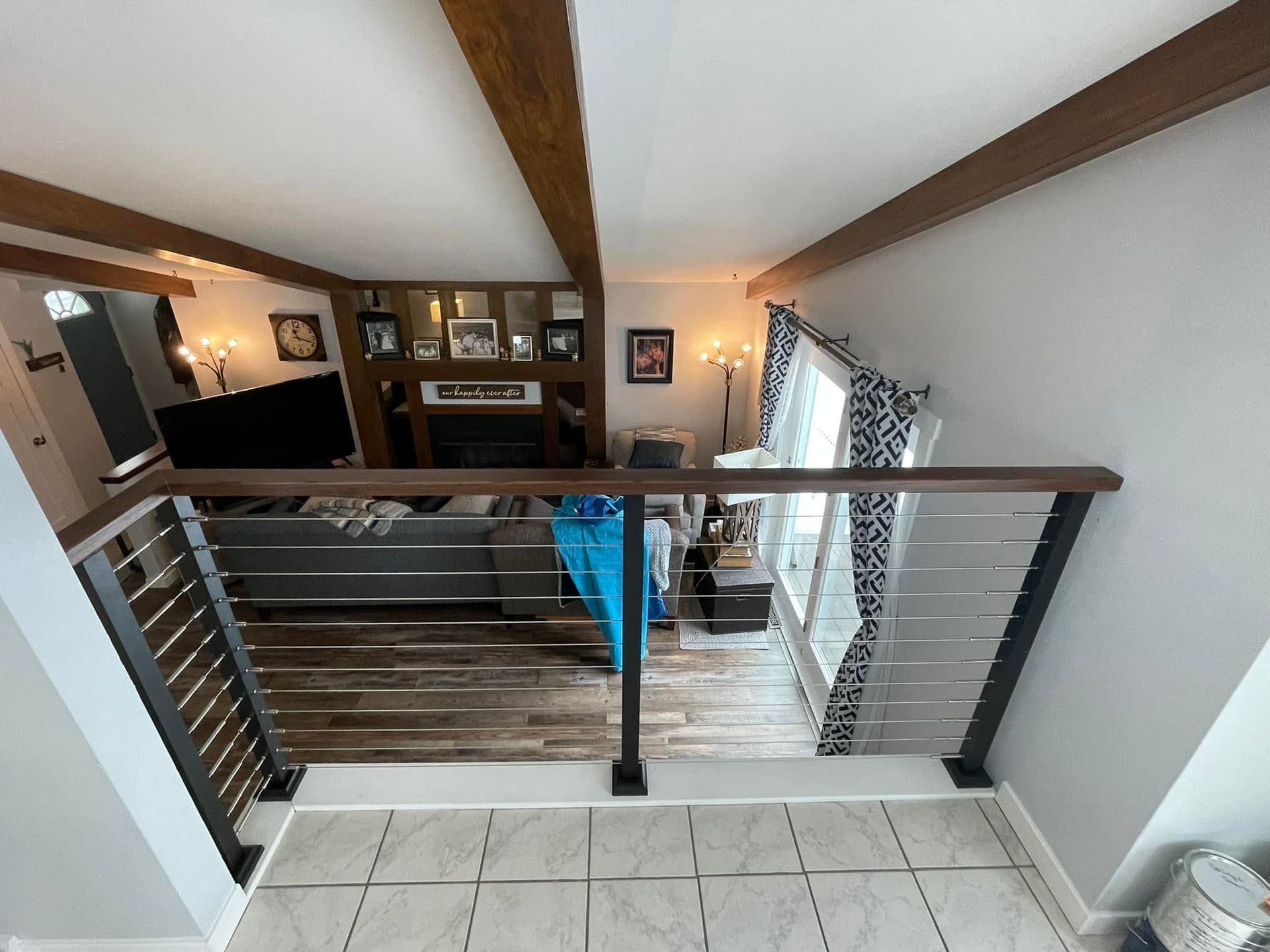 Interior balcony overlooking living room with wood beams, railing, and tiled floor