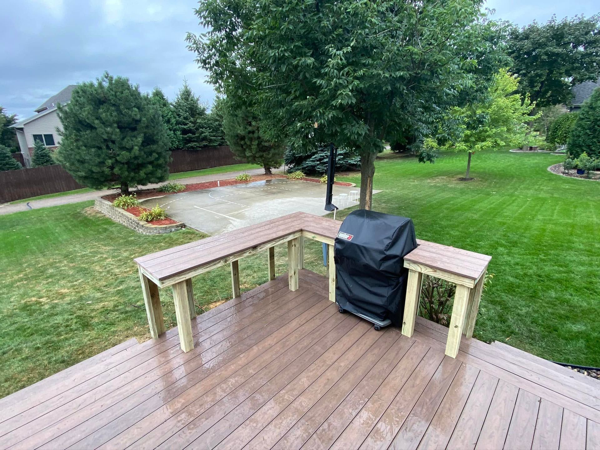 Wooden deck with benches and a covered grill overlooking a grassy backyard and garden path