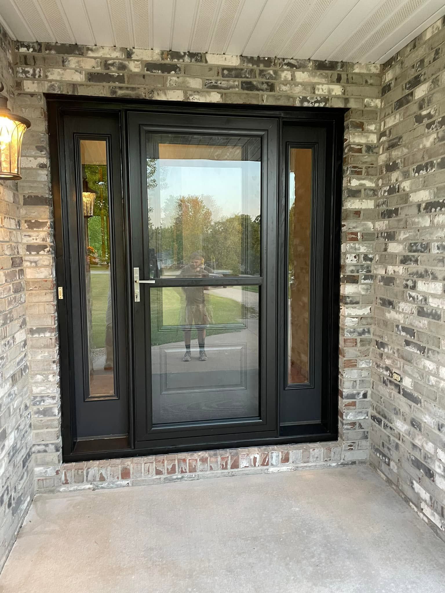 Black front entry door with side windows under a covered brick porch