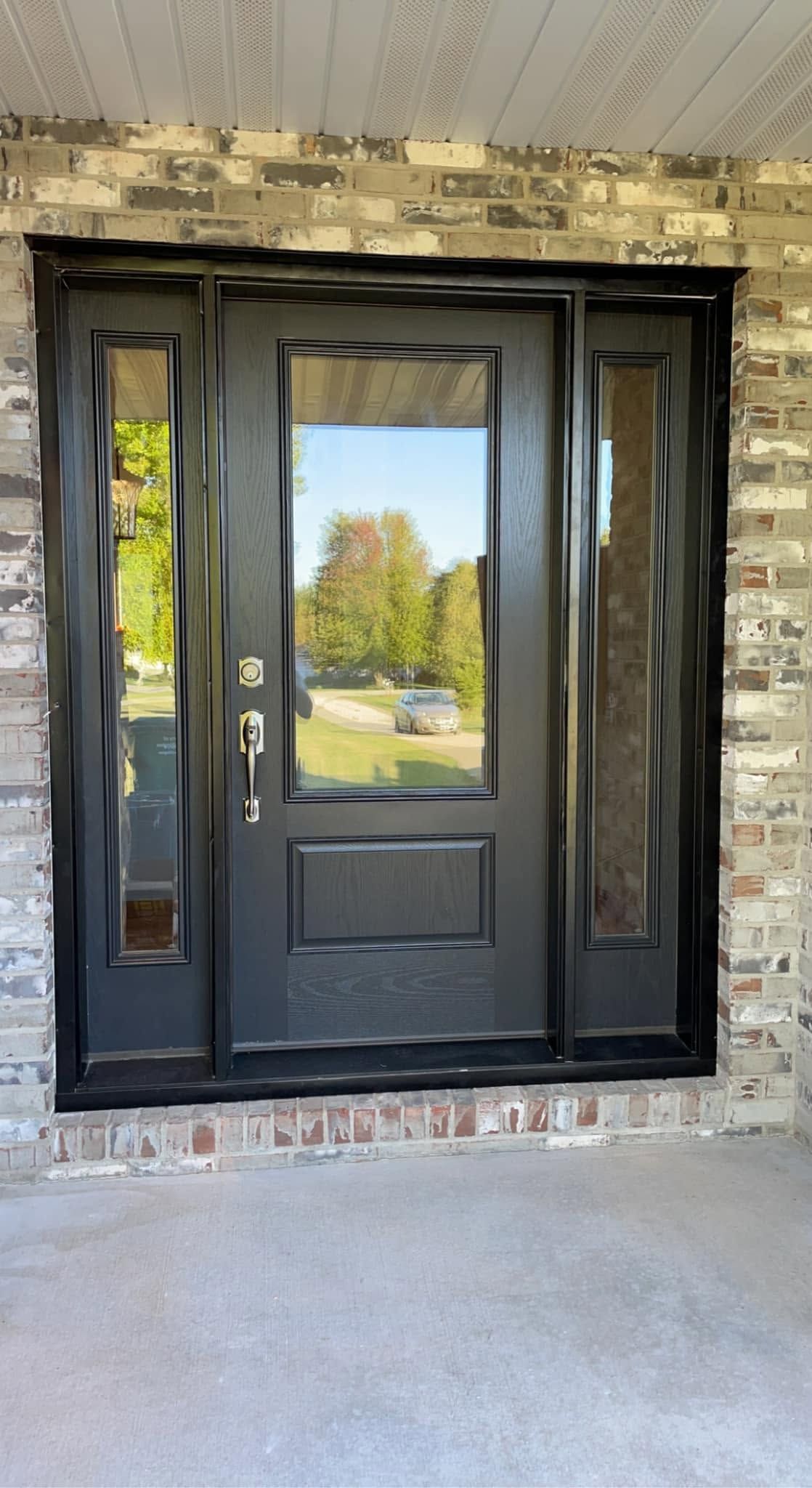 Black front door with sidelights set in a stone exterior wall and concrete porch.