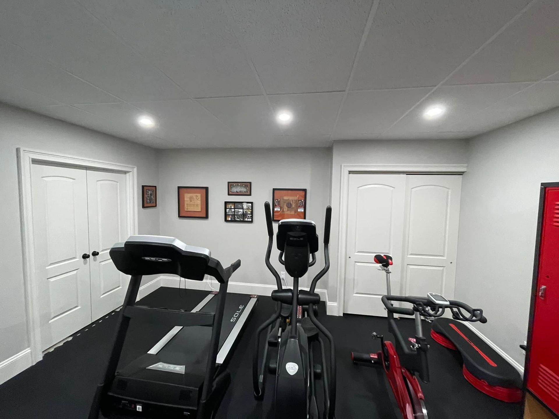 Home gym with a treadmill, stationary bike, rowing machine, and weights in a gray room.