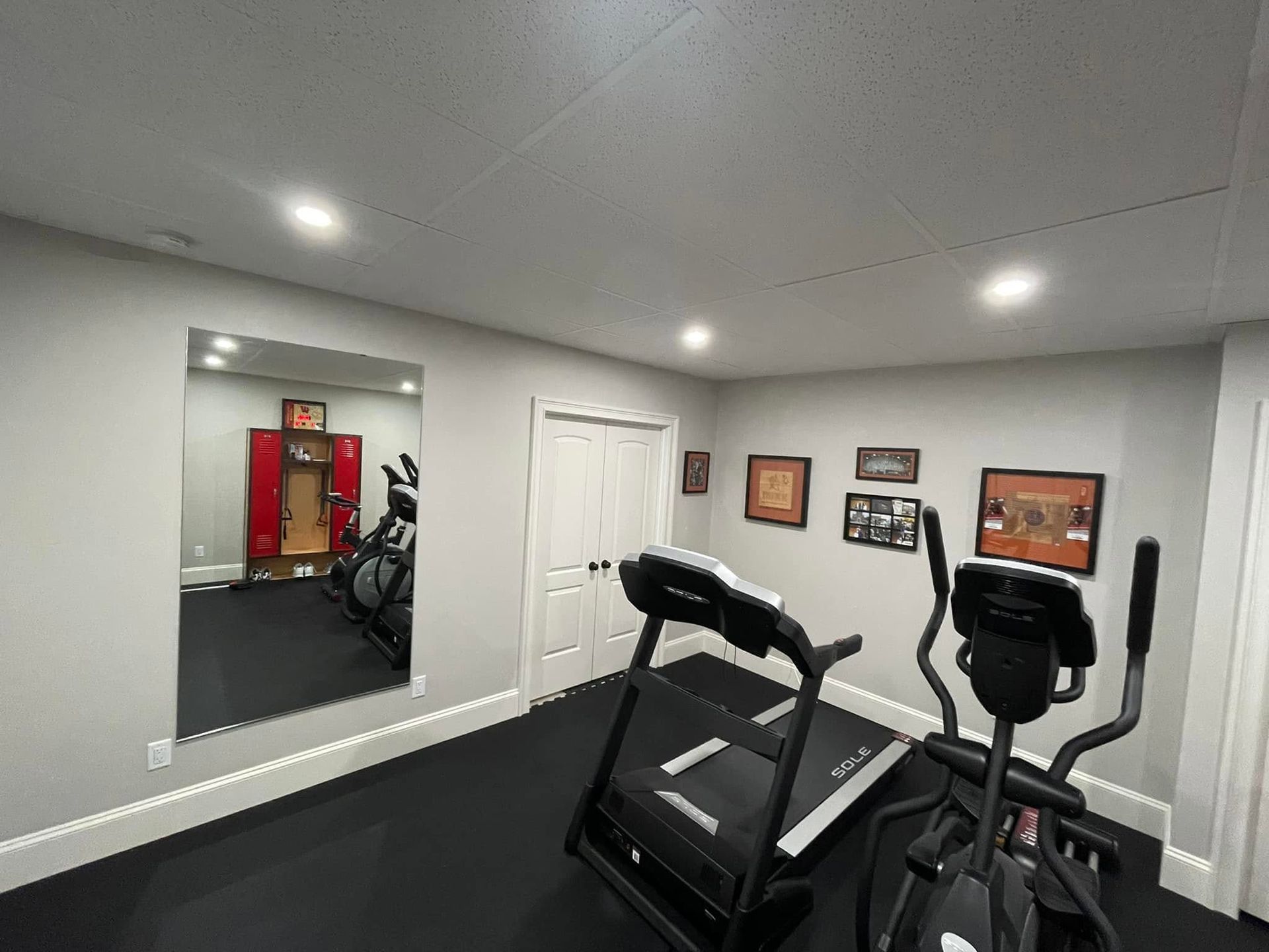 Home gym with treadmill and elliptical in a mirrored room with white doors and framed wall art