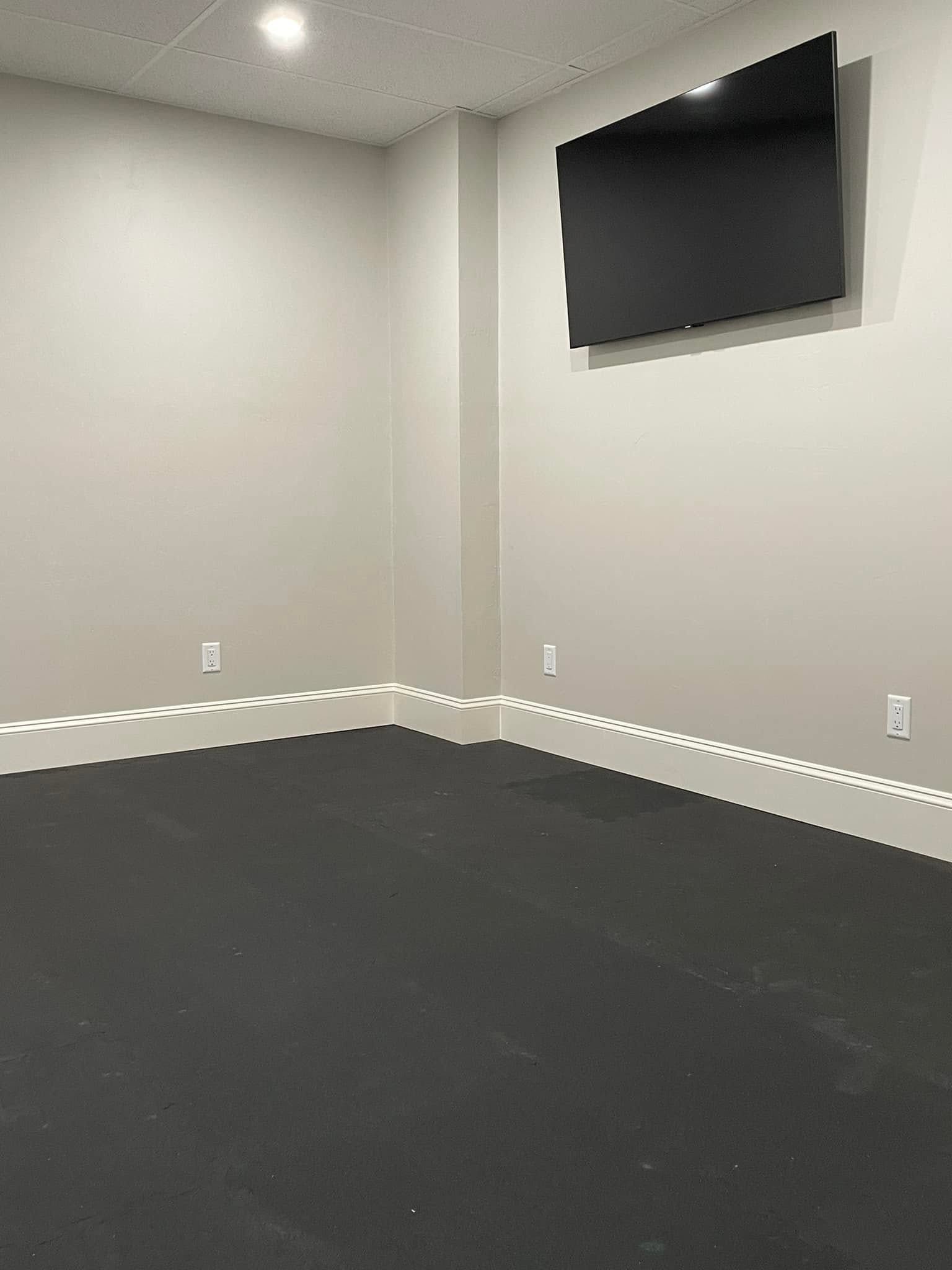 Empty room with gray carpet, white walls, and a wall-mounted TV in the corner.
