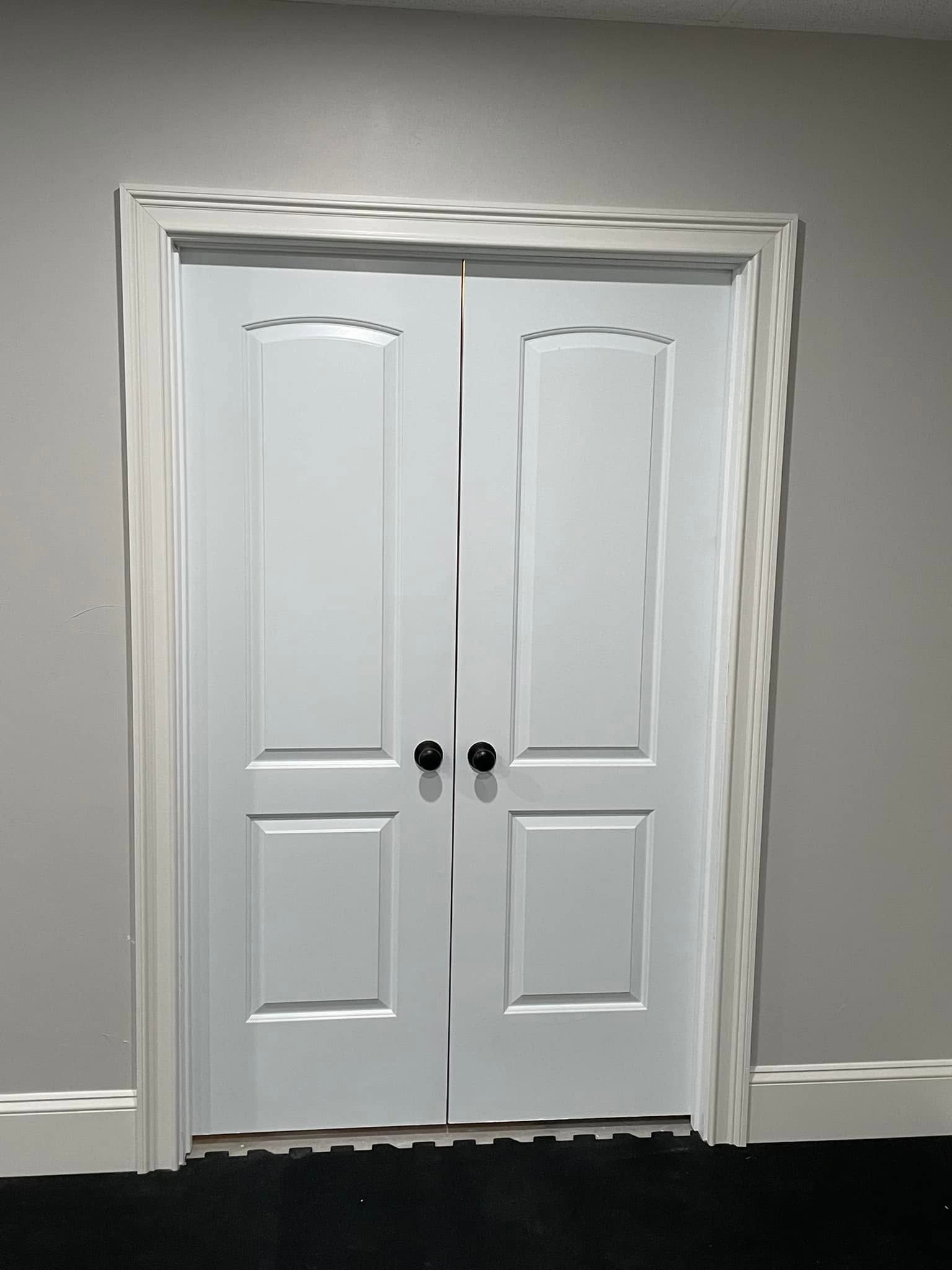 White double closet doors with black knobs set in a gray wall.