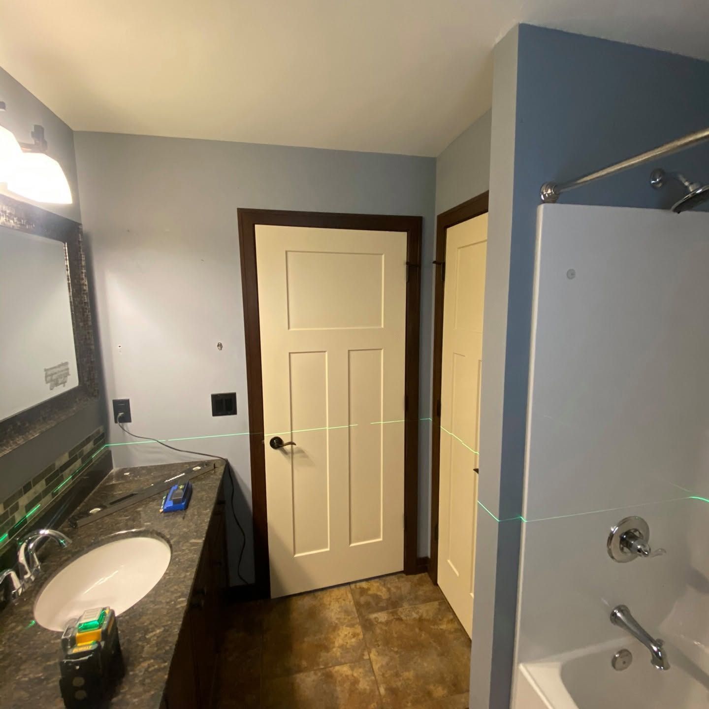 Bathroom with granite vanity, sink, mirror, blue walls, and a shower stall beside two closed doors.