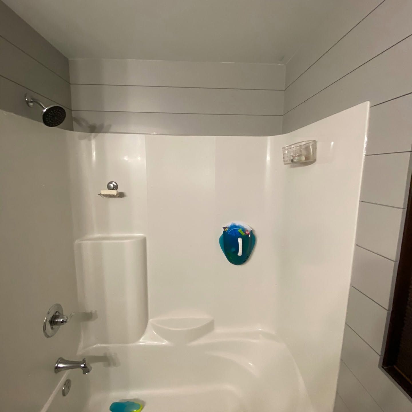 Small white bathtub and shower stall with gray shiplap walls and a blue soap holder on the wall