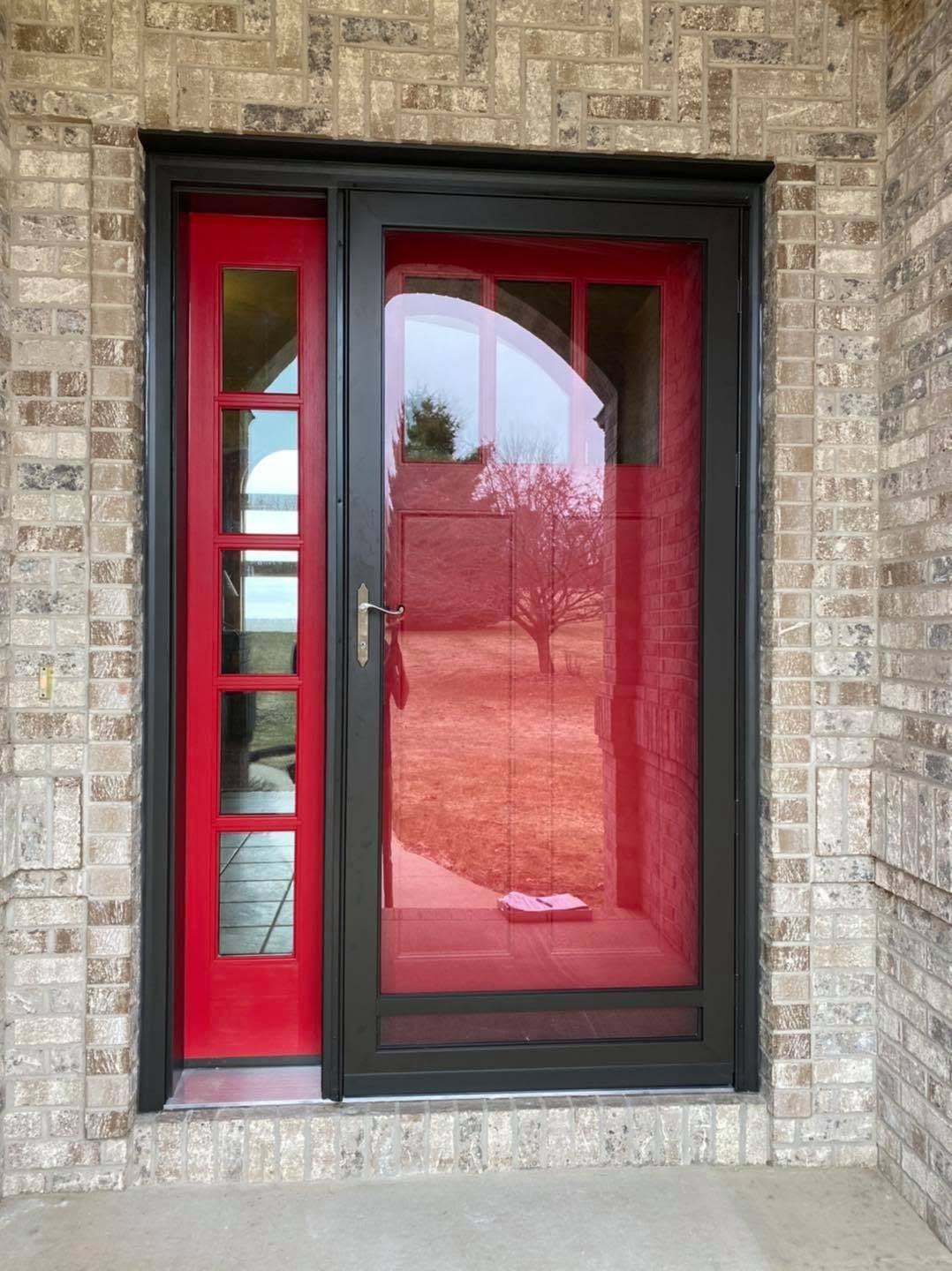 Red front door with glass panels set in a stone brick exterior wall