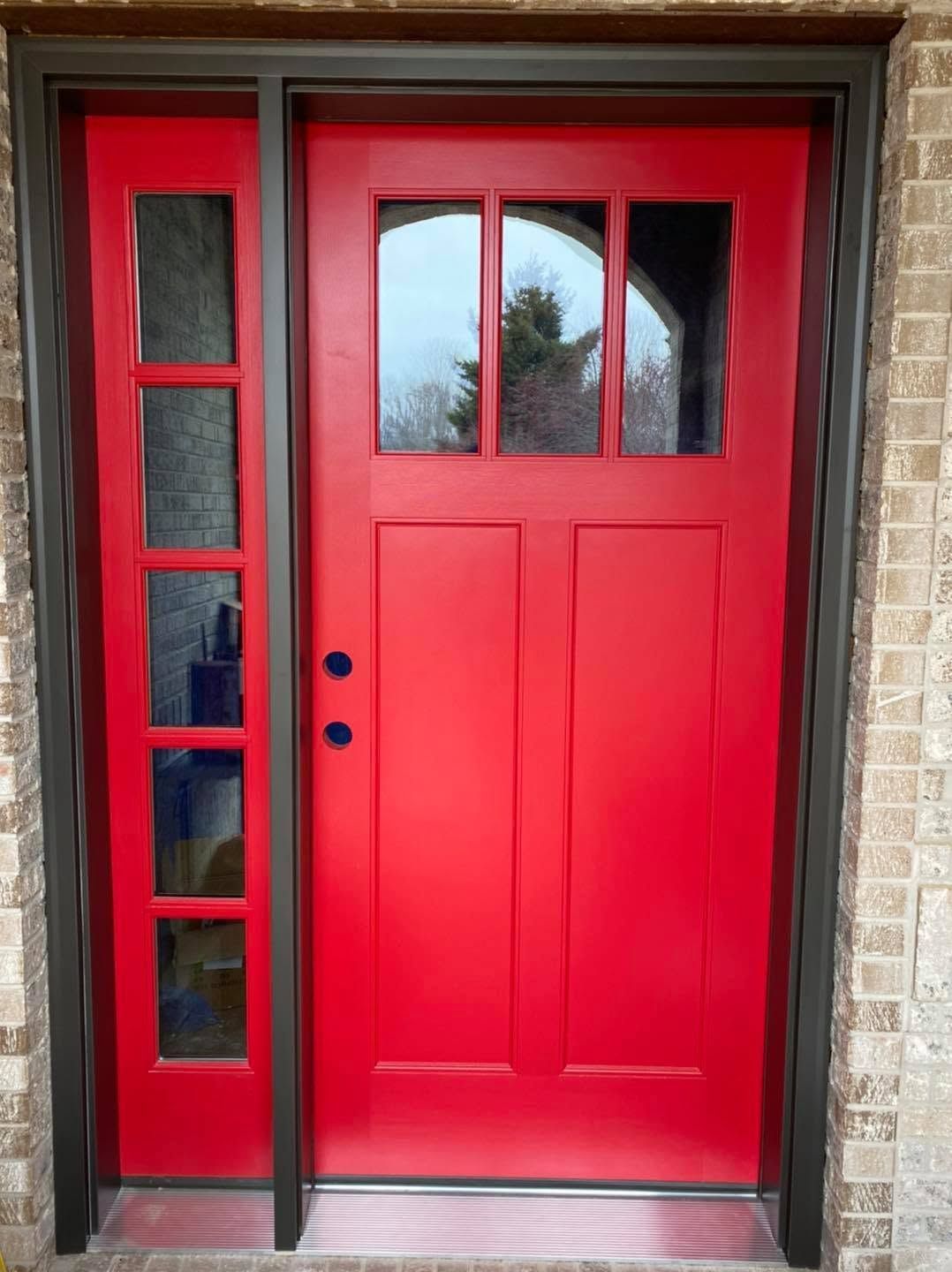 Bright red front door with narrow side windows and a glass transom in a brick entryway