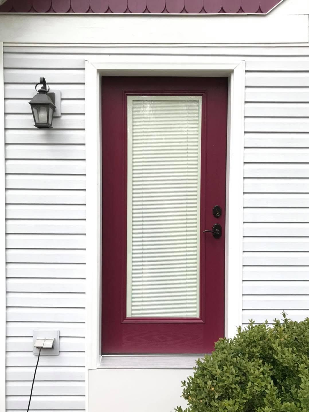White house exterior with burgundy front door, wall lantern, and green bushes