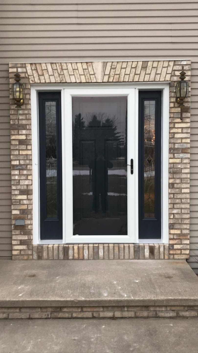 Front entrance with a black door, sidelights, brick facade, and a small concrete stoop.