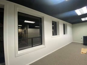 Empty office room with white walls, windows, gray carpet, and ceiling lights