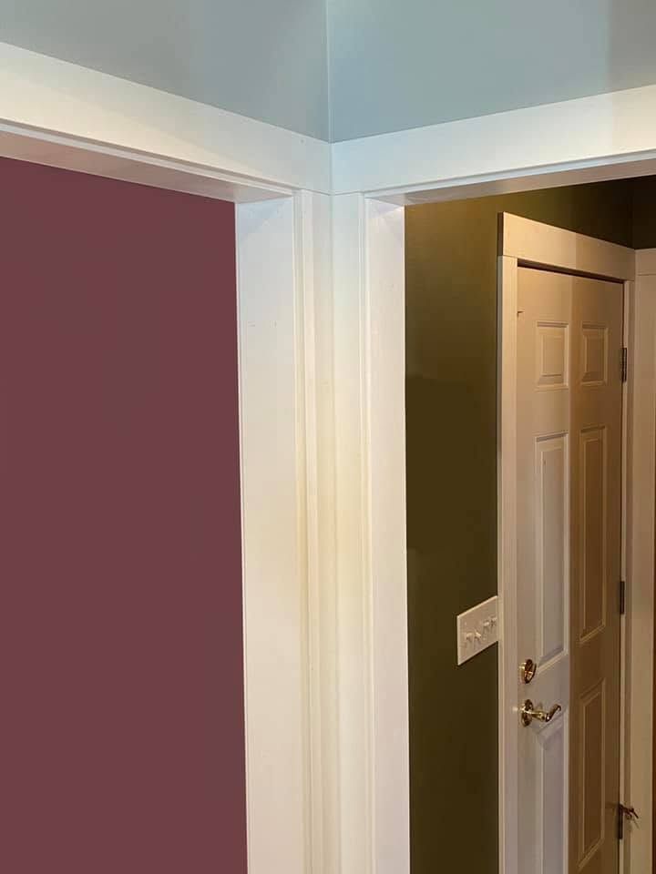 Interior hallway corner with mauve and olive walls, white trim, and an open door to a room.
