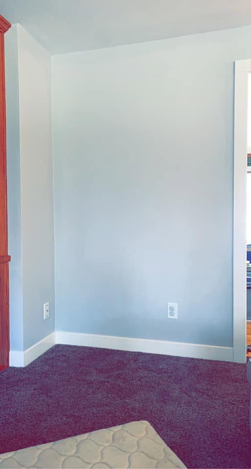 Empty light gray room with white trim, red doorway, and dark carpet floor.