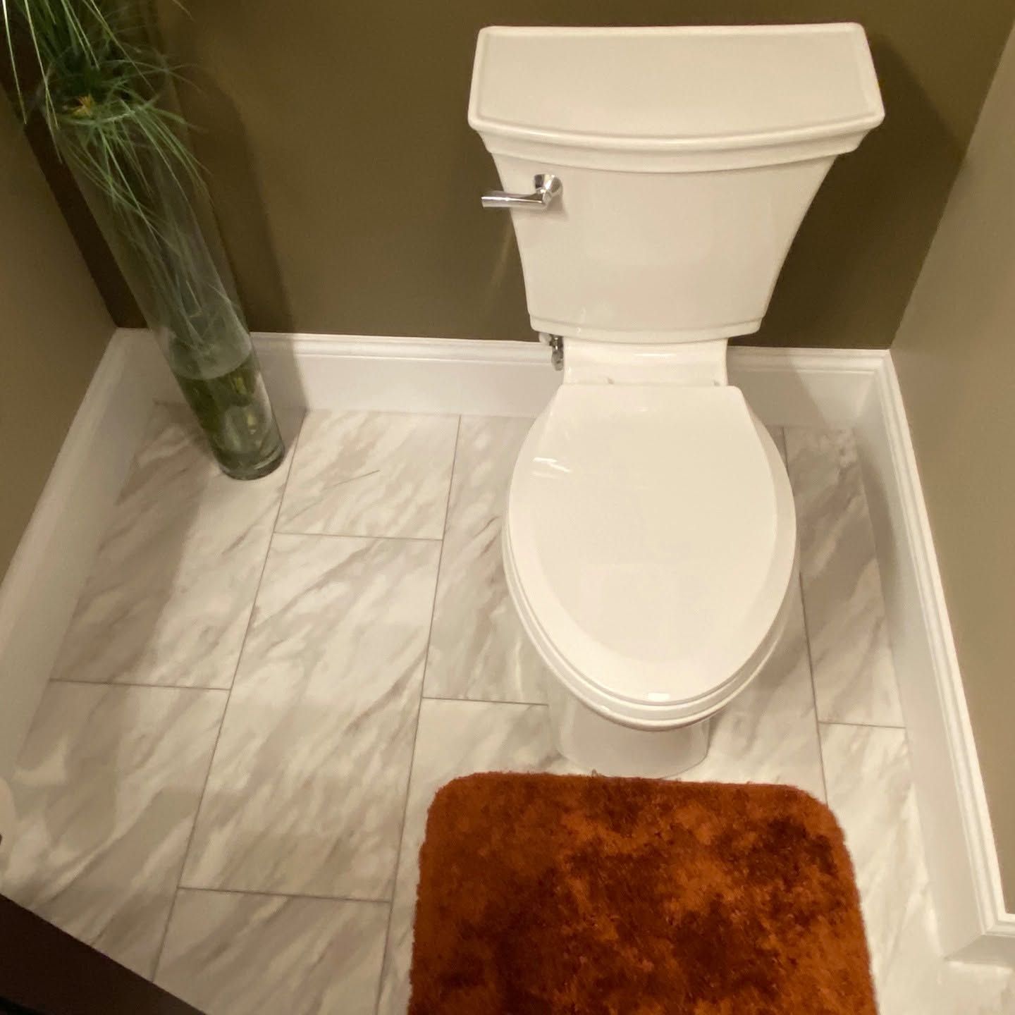 Compact bathroom with a white toilet, marble-look tile floor, and brown bath mat.