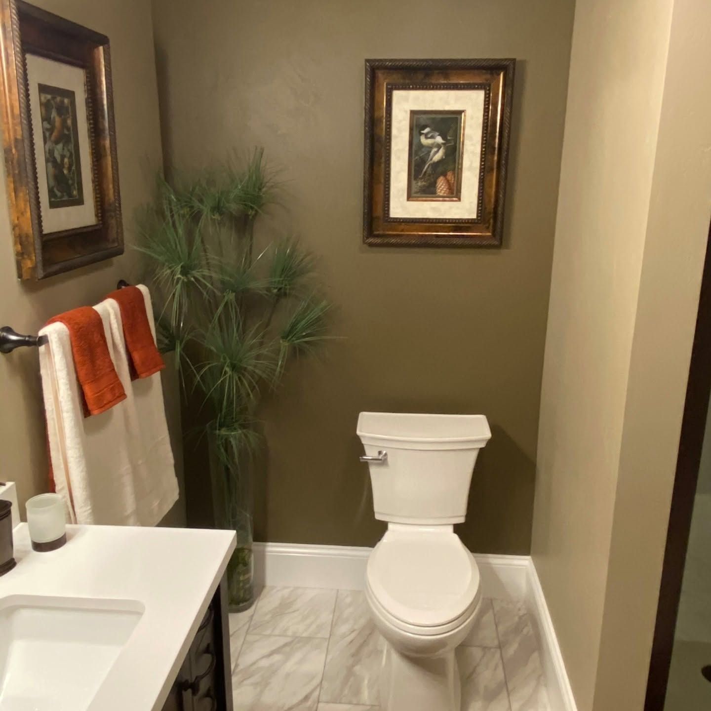 Small bathroom with a white toilet, sink, mirror, and framed wall art in beige tones.