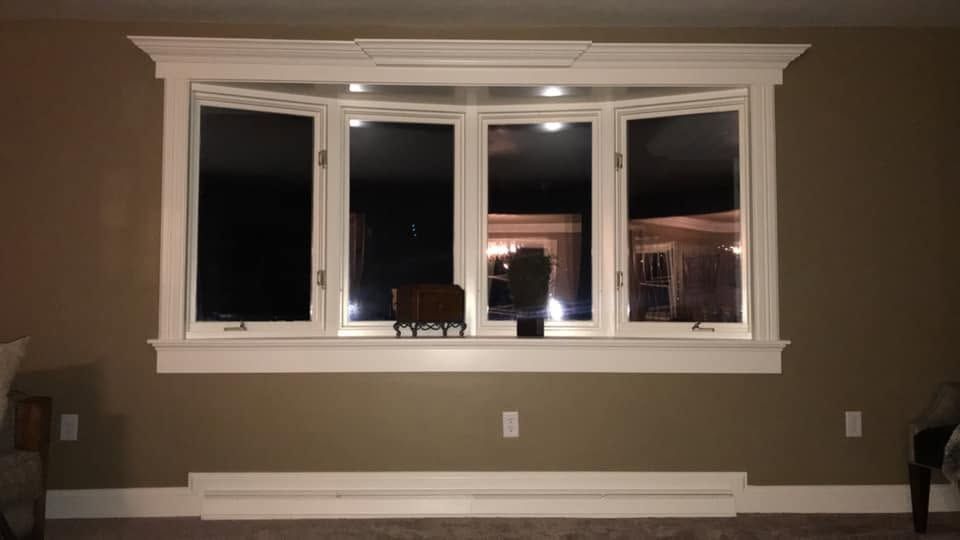 Living room wall with large white-trimmed window, brown walls, and a low white bench beneath it.